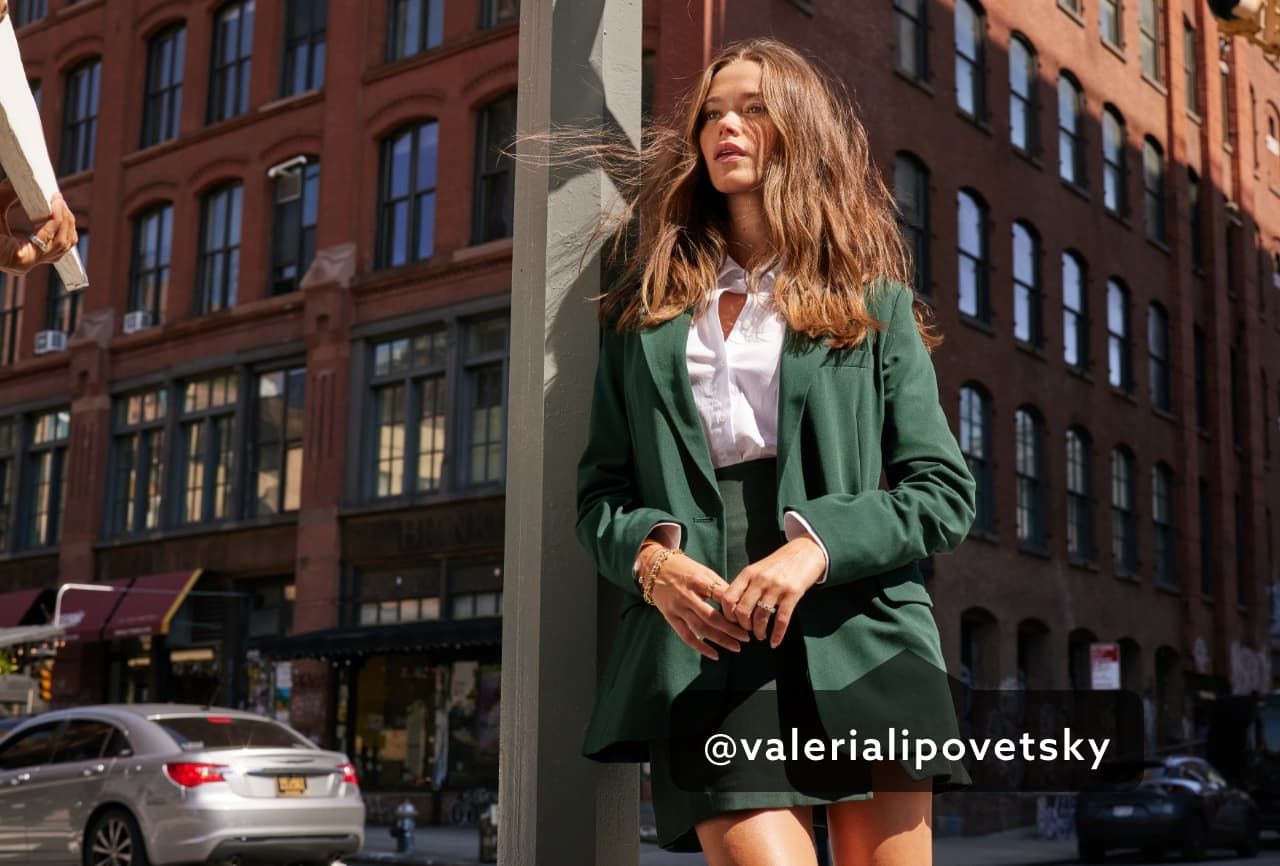 A model wears a green mini skirt with a matching green blazer and white button up shirt.
