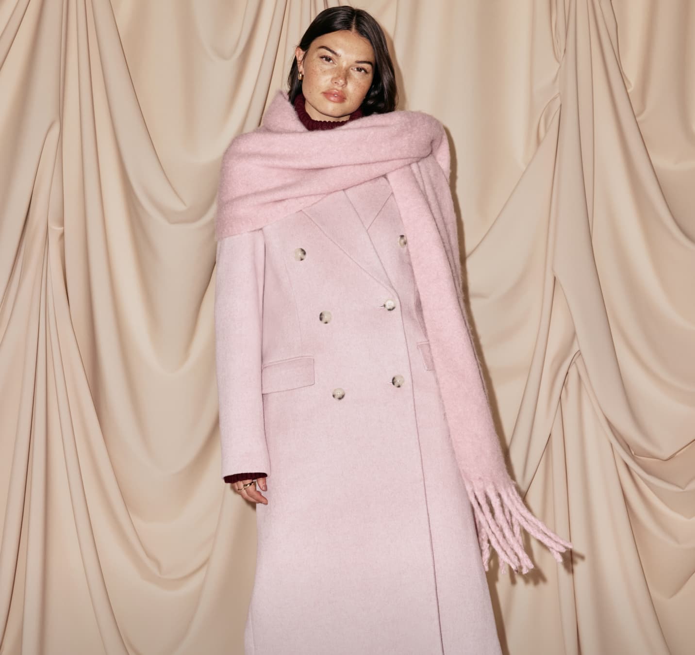 Model is wearing a pink wool coat and a pink scarf.