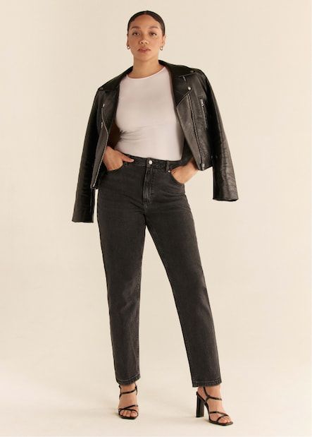 Une mannequin porte le jean « mom » Claudia en gris foncé avec un justaucorps blanc et un blouson de moto en faux cuir.