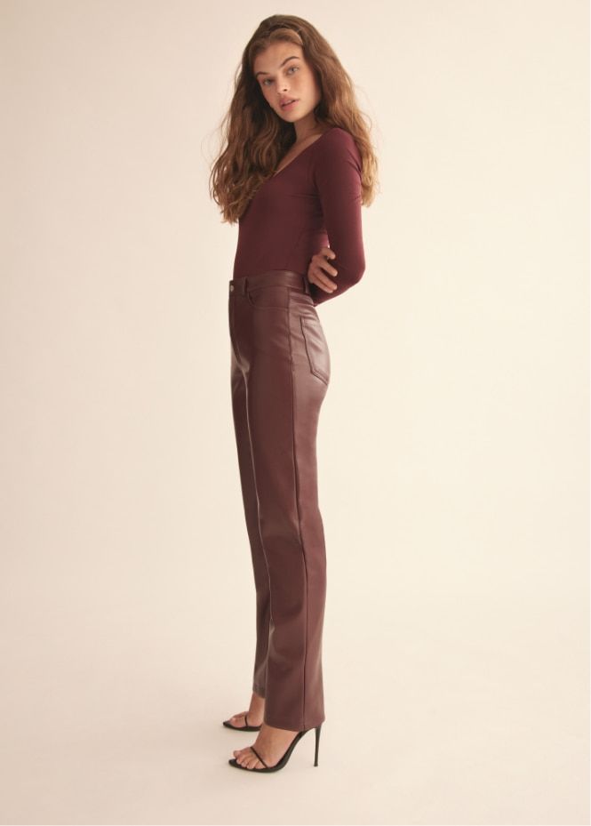 Une mannequin porte un pantalon droit ajusté en faux cuir bourgogne et un haut bourgogne.