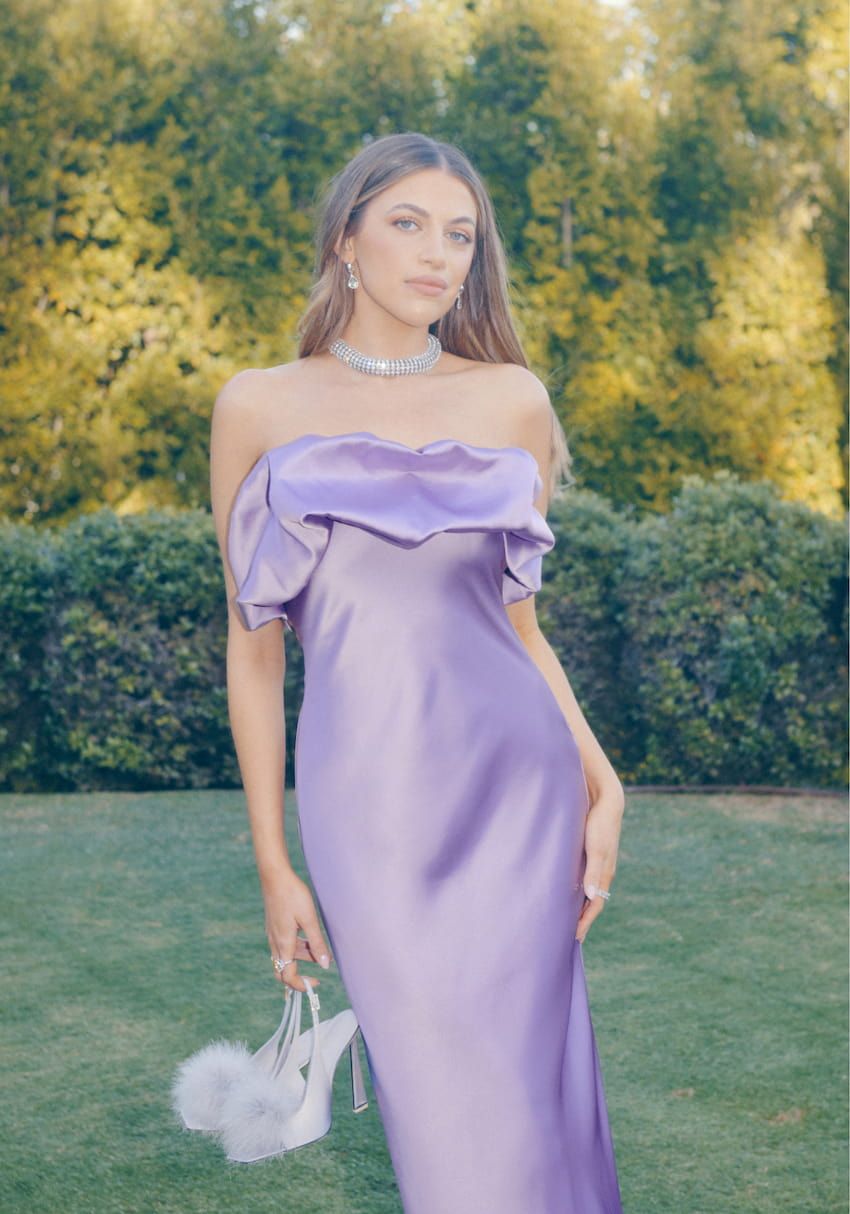 An influencer wears a purple off-the-shoulder satin dress.
