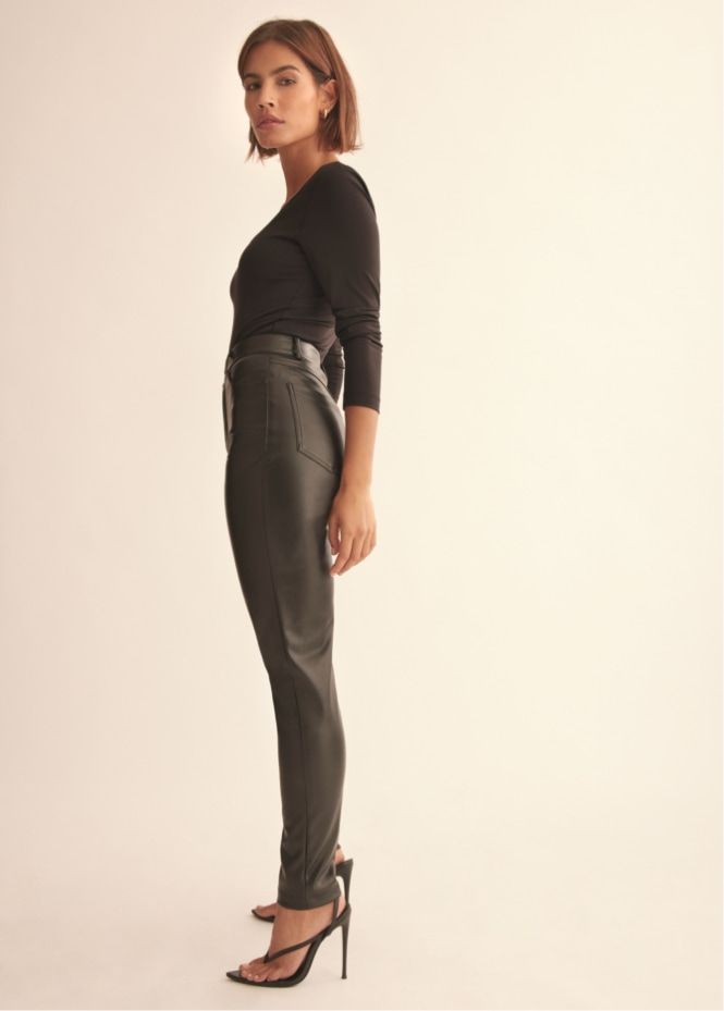 A model wears black faux leather skinny pants with a black top.