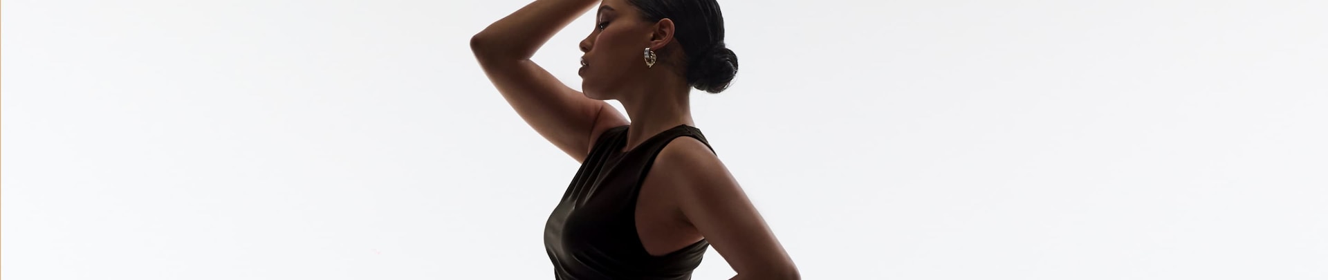 Model is wearing gold earrings and a black plunge tank top.