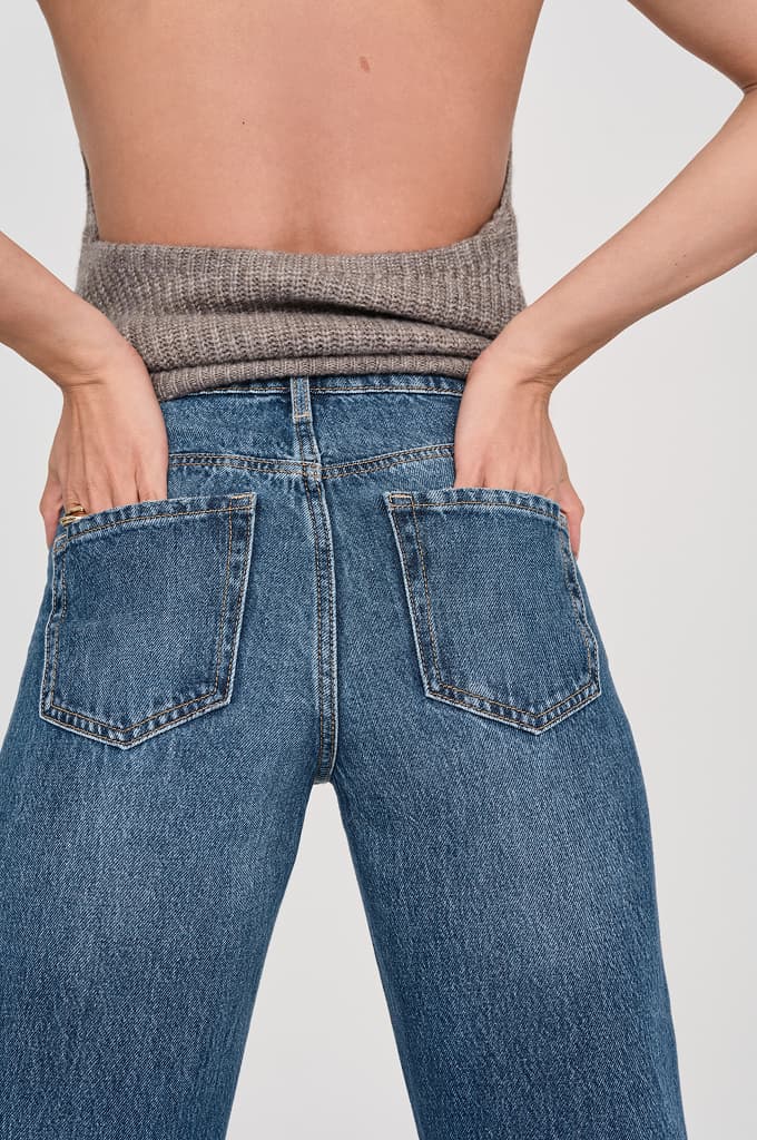 Model is wearing a brown knit halter top and blue wide leg jeans.