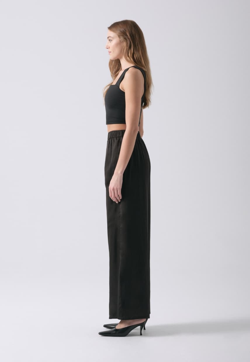A model wears black wide leg satin pants with a black tank top.