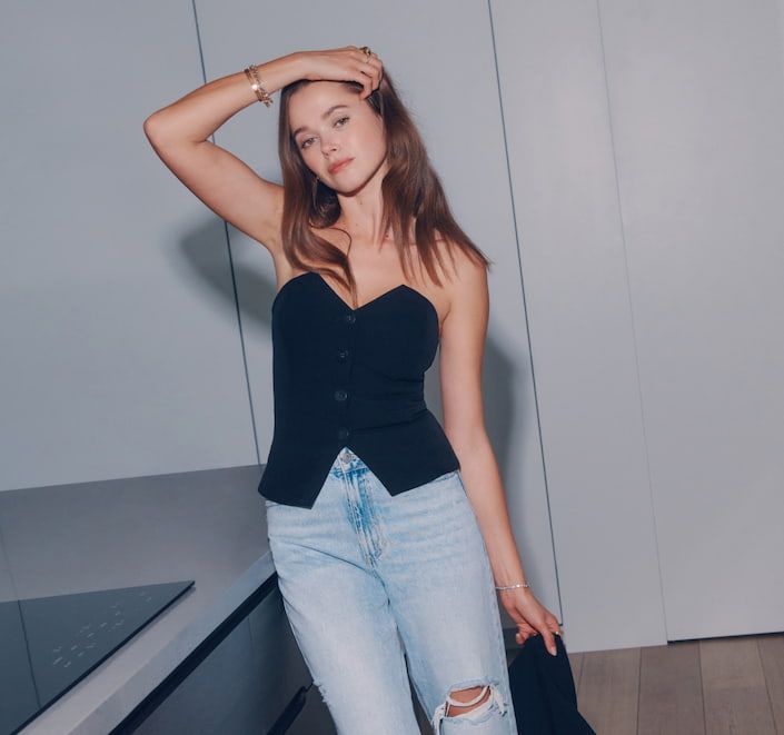 Valeria Lipovetsky wears a black buttoned bustier top with blue distressed mom jeans.