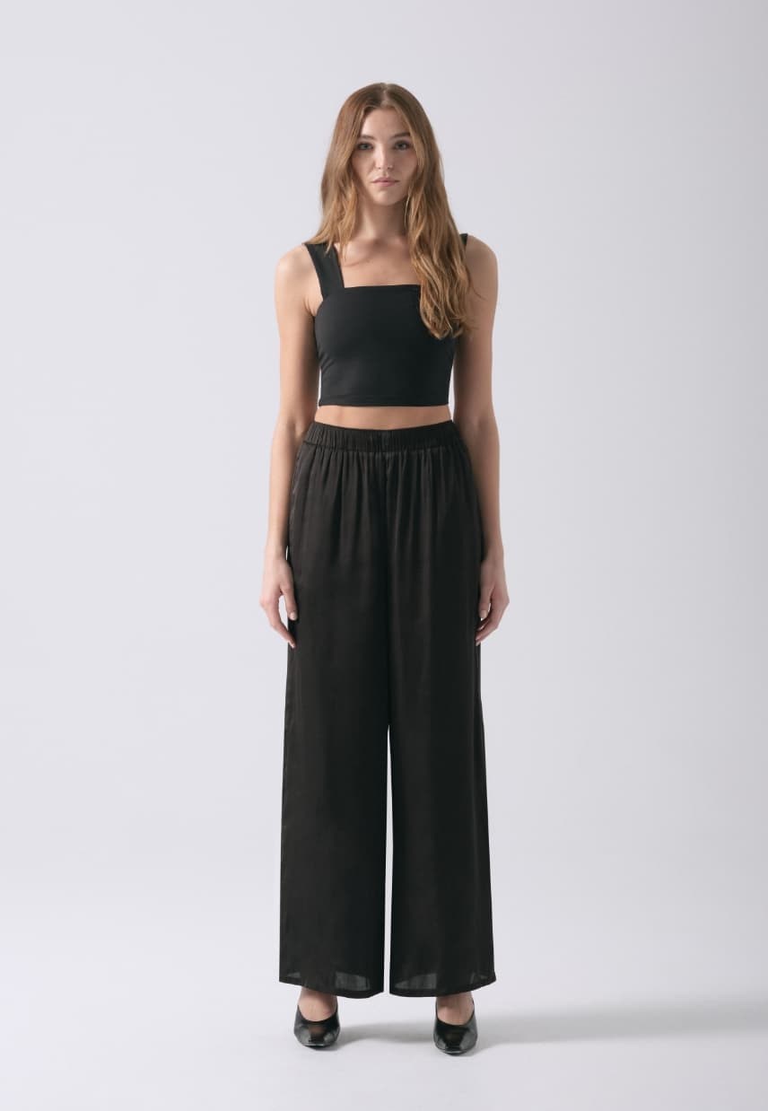 A model wears black wide leg satin pants with a black tank top.