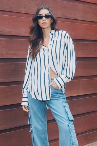 A model wears a white and black striped button down shirt with blue cargo jeans.