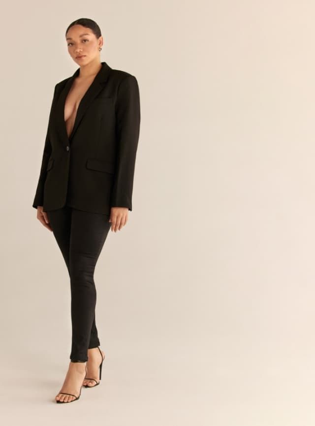 Une mannequin porte un jean skinny noir avec un veston noir.