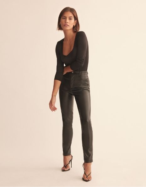 a model wears black faux leather skinny pants with a black top .