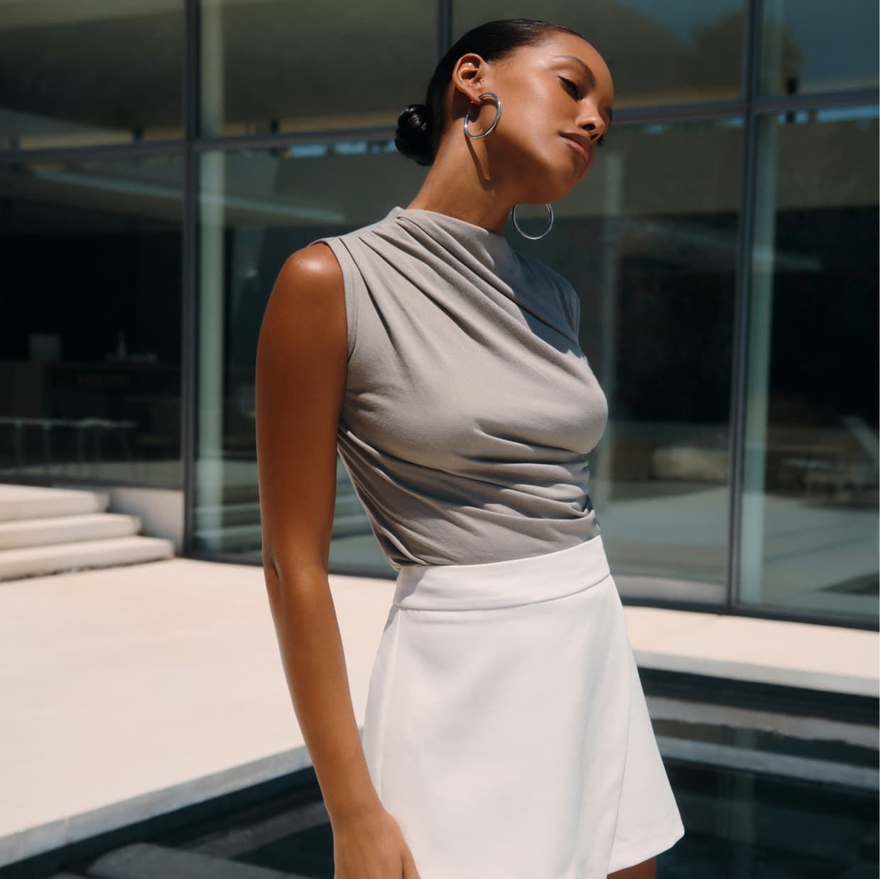 A model wears a sleeveless ruched grey top with a white mini skirt.