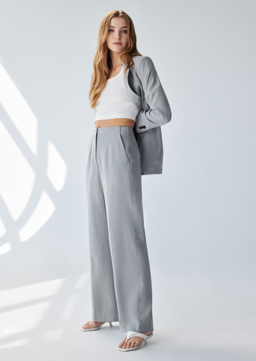 A model wears grey straight leg pants with a white tank top and grey blazer.