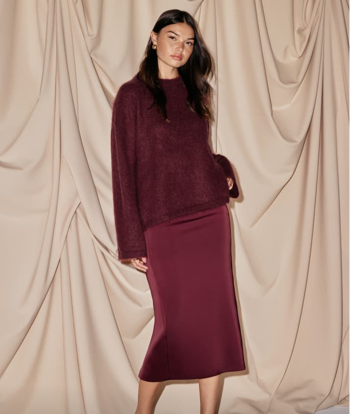Model is wearing a burgundy sweater with a burgundy satin maxi skirt.
