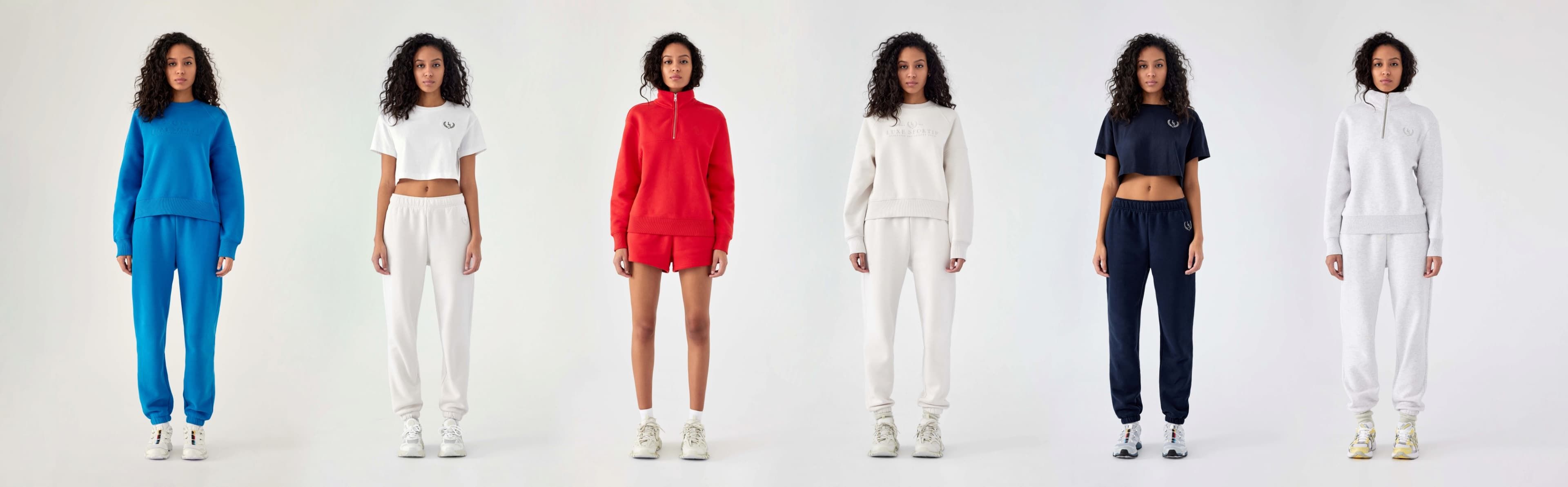 A model wears the blue crewneck and sweatpant set, the white crop t-shirt and white sweatpant, the red crewneck and short set, the white crewneck and sweatpant set, a black crop t-shirt and black sweatpant, and a white zip-up hoodie and sweatpant set.