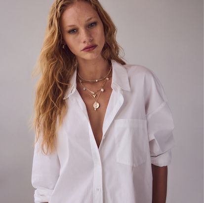 Une mannequin prend la pose dans une blouse blanche et des colliers.