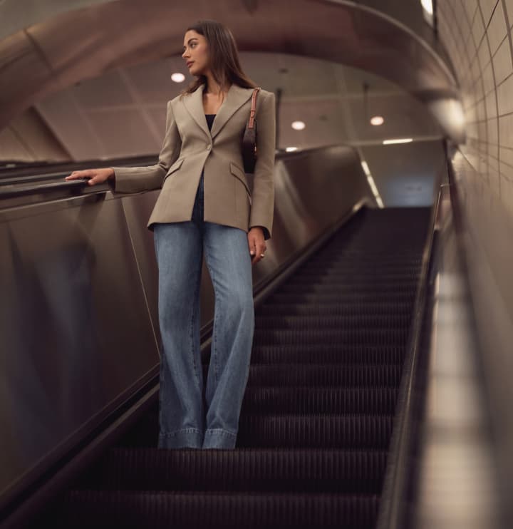 Model is wearing a brown cinched blazer with light blue jeans.