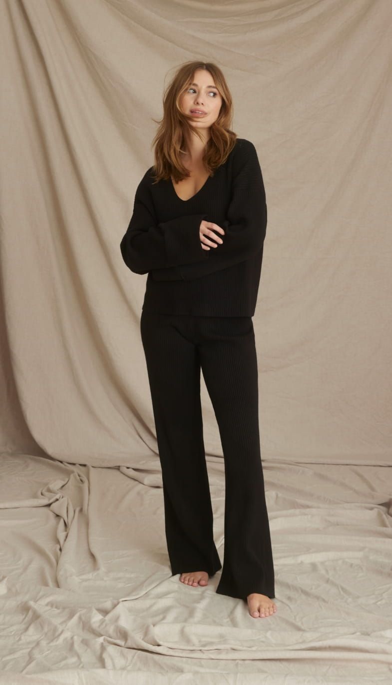 A model wears a black v-neck sweater with matching sweatpants.