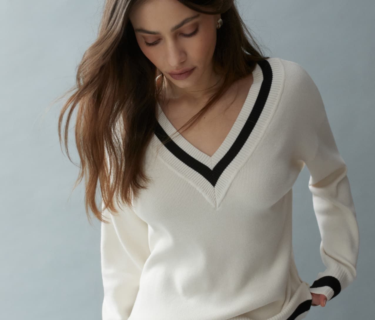 Model is wearing a white V-neck sweater and black pants.