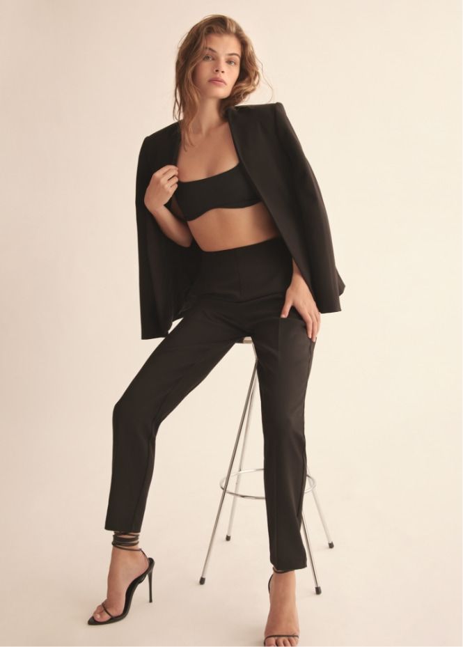 A model wears black slim pants with a black bra top and matching blazer.