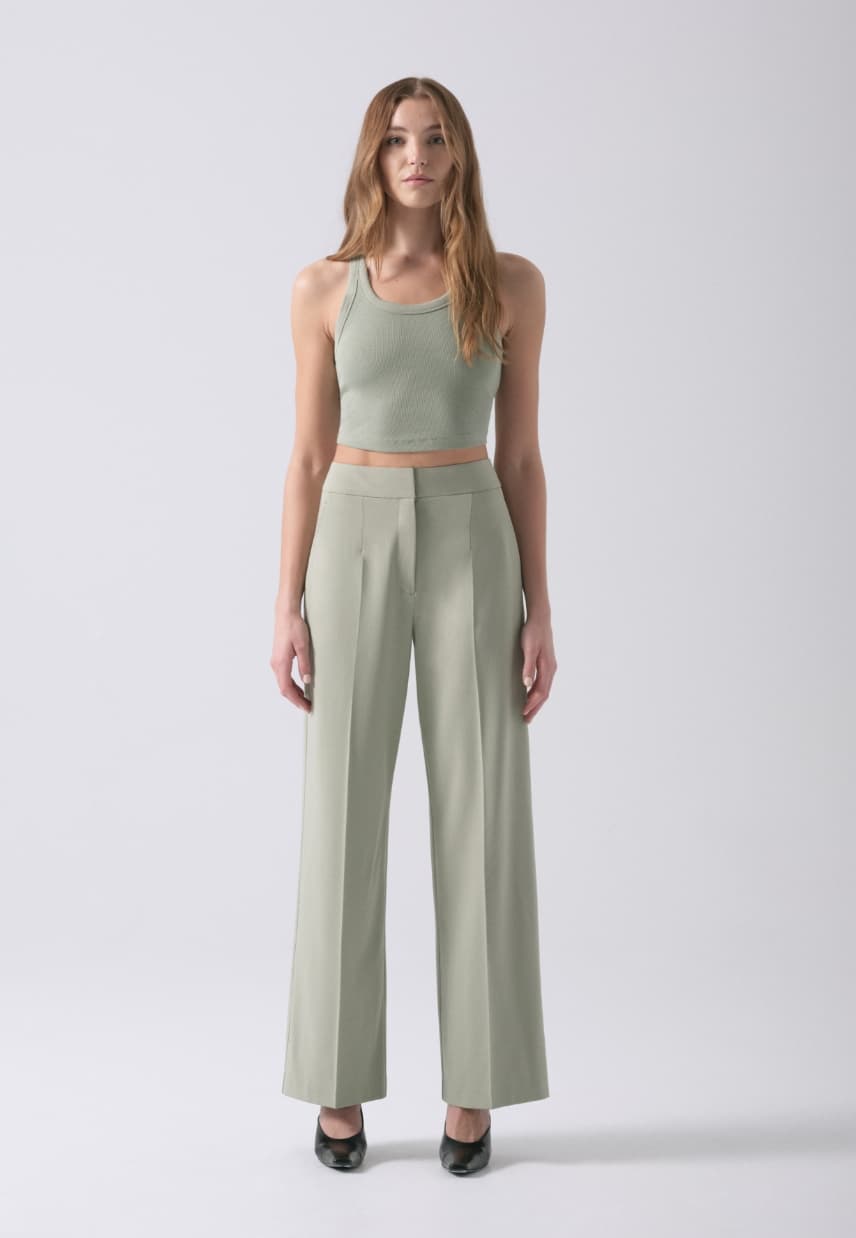 A model wears khaki green straight leg pants with a khaki green tank top.