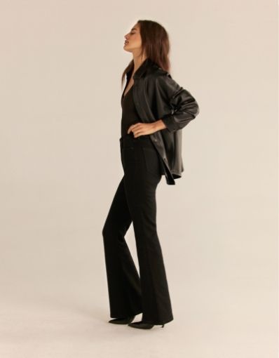 A  model wears black flared leg jeans with a black faux leather shacket.
