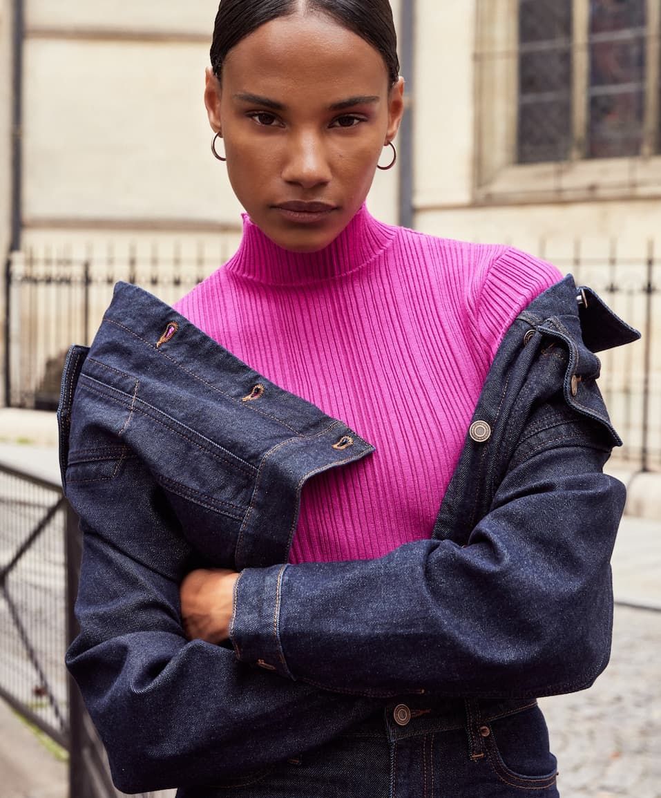 A model wears a hot pink mock-neck top and a denim jacket.