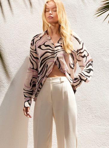 A model wears a geometric print button-down shirt with white wide-leg pants.