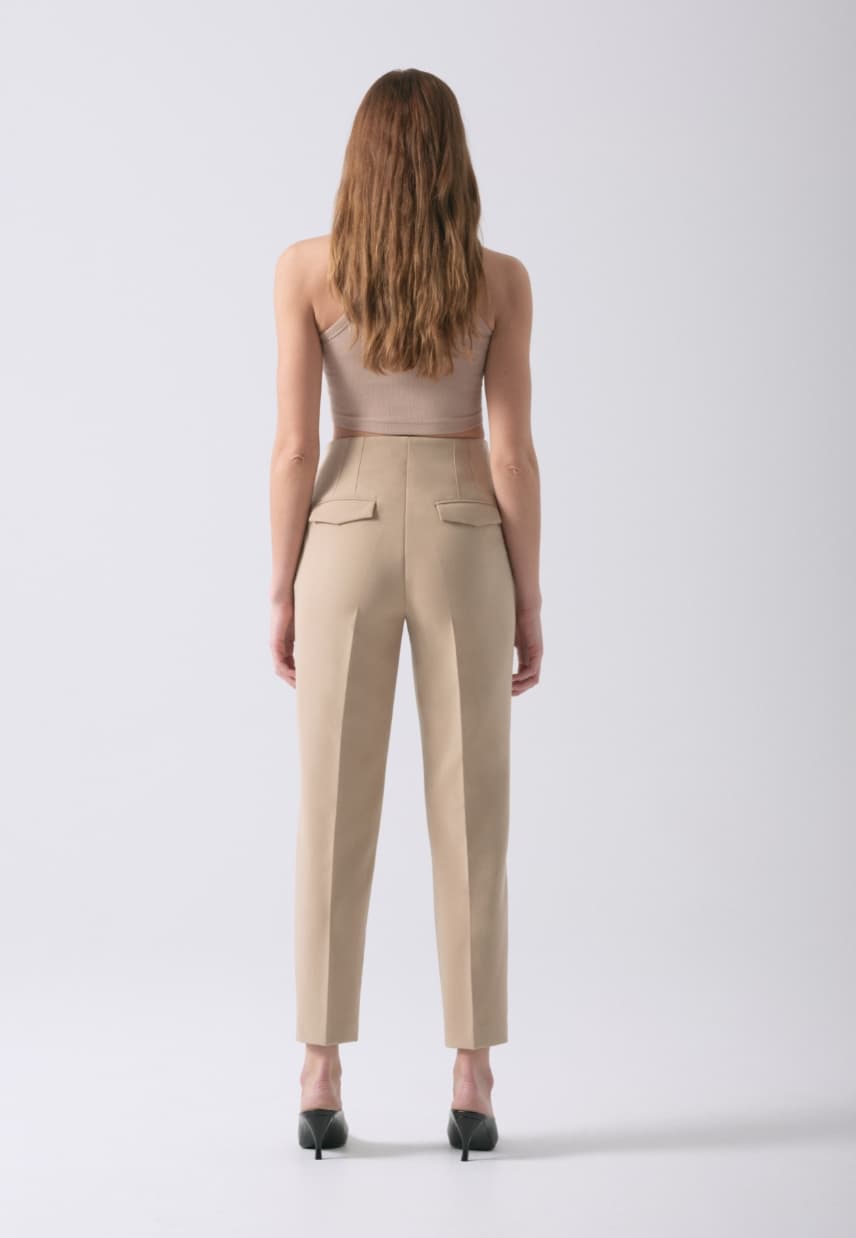 A model wears beige slim leg pants with a beige tank top.