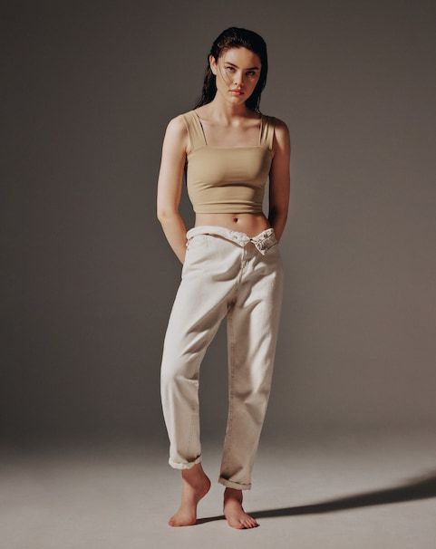A model wears a wide strap squareneck beige sculpt'd tank top with white jeans.