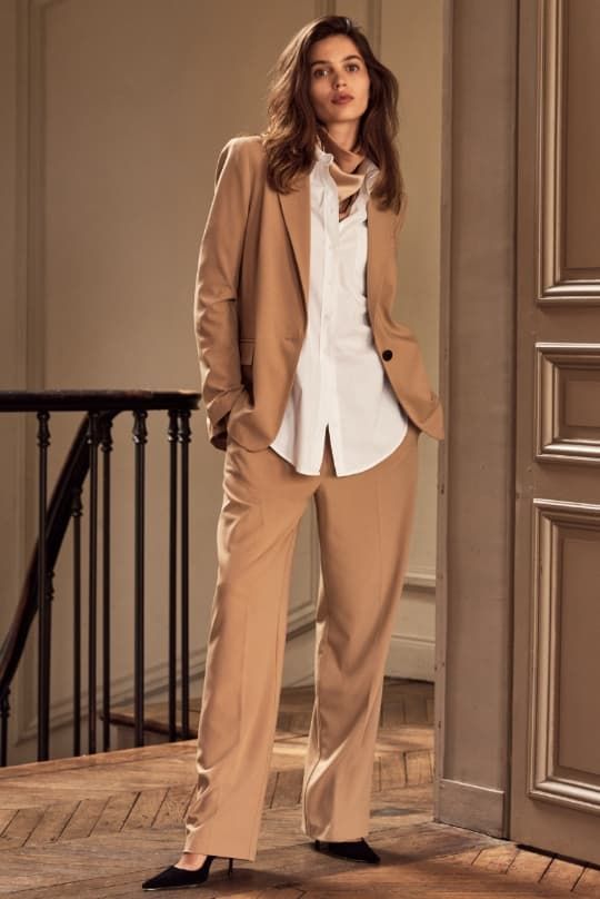 A model wears beige straight leg pants with a matching beige blazer and a white button down shirt.