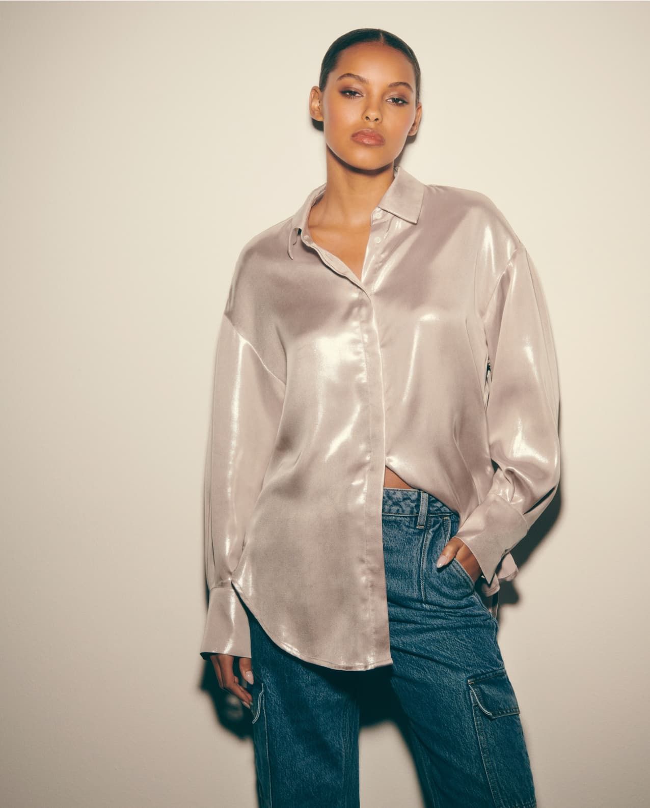 A model wears a metallic silver button down shirt with blue jeans.