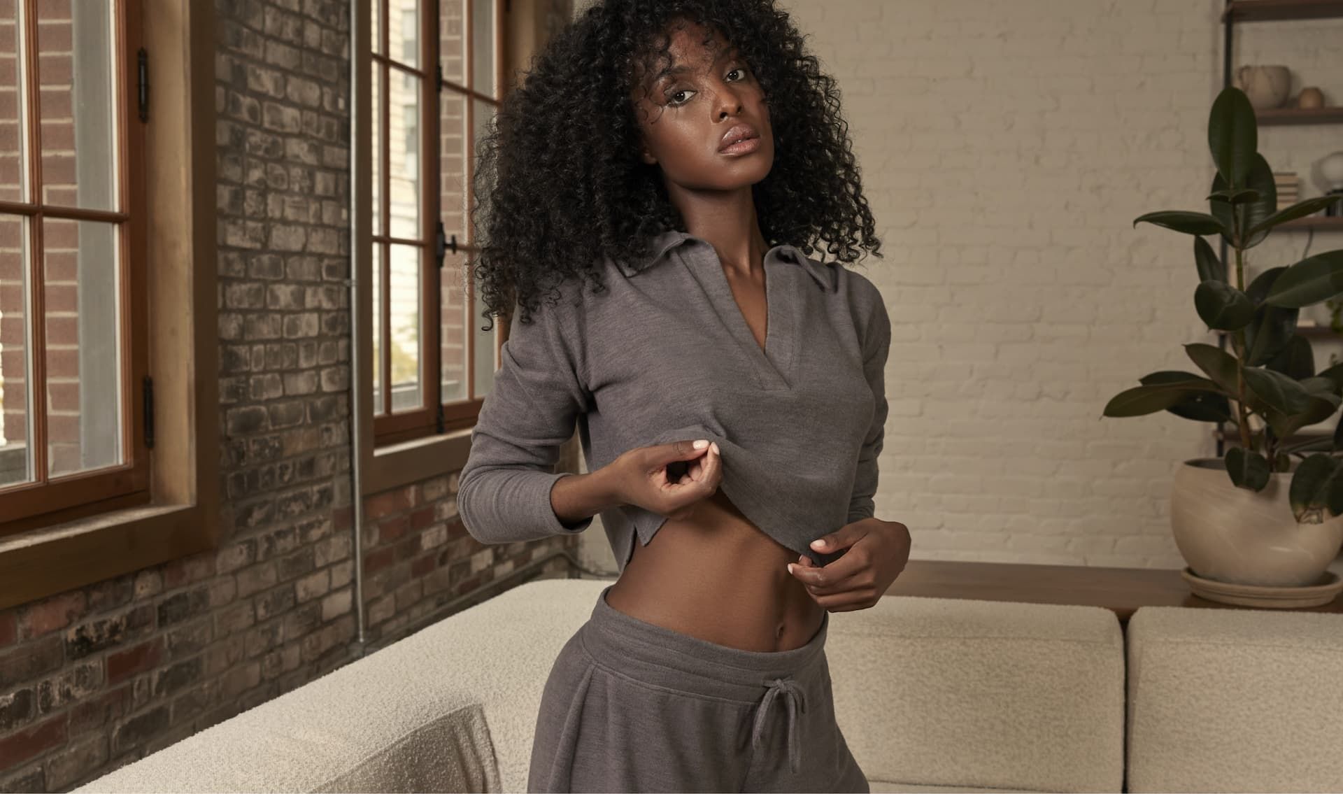 A model wears a grey long sleeve lounge collared shirt with matching grey lounge shorts.
