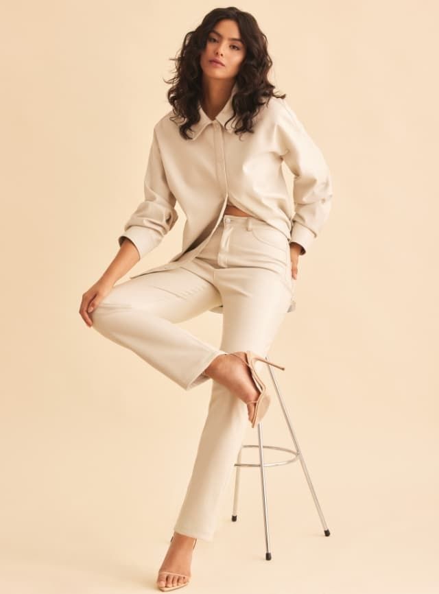 A model wears a beige faux leather button down shacket with matching beige faux leather pants.