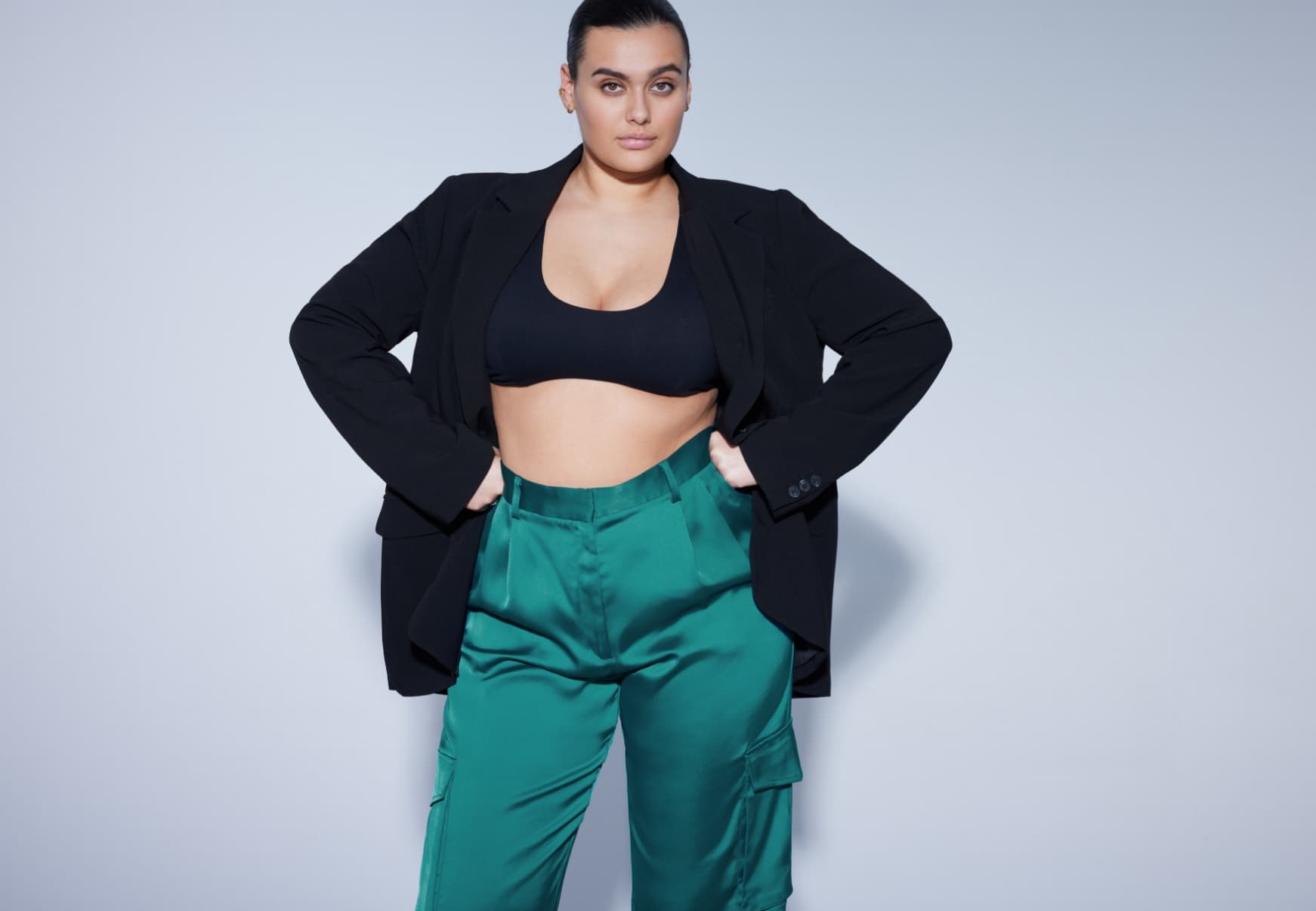 A model wears blue satin cargo pants with a black bra top and black blazer.