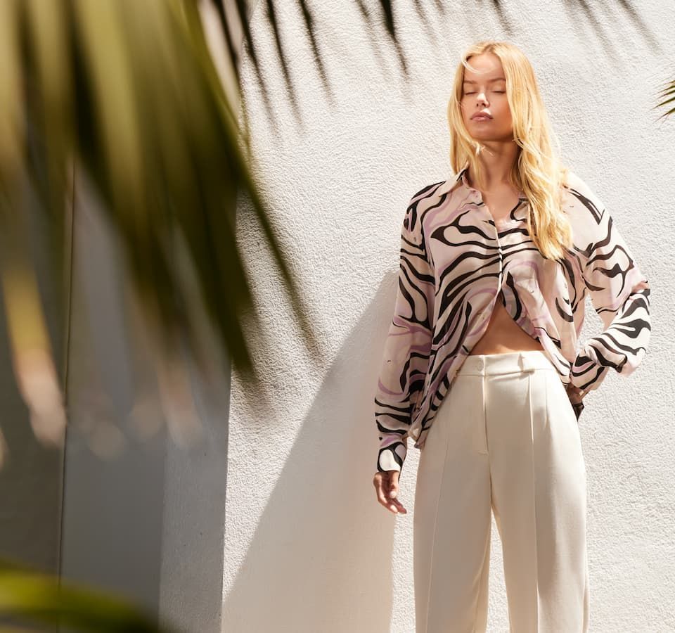 A model wears a printed chiffon button-down shirt with white pleated-front pants.