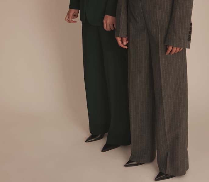 Une mannequin porte un pantalon habillé vert forêt et l'autre mannequin porte un pantalon habillé gris foncé à fines rayures. 