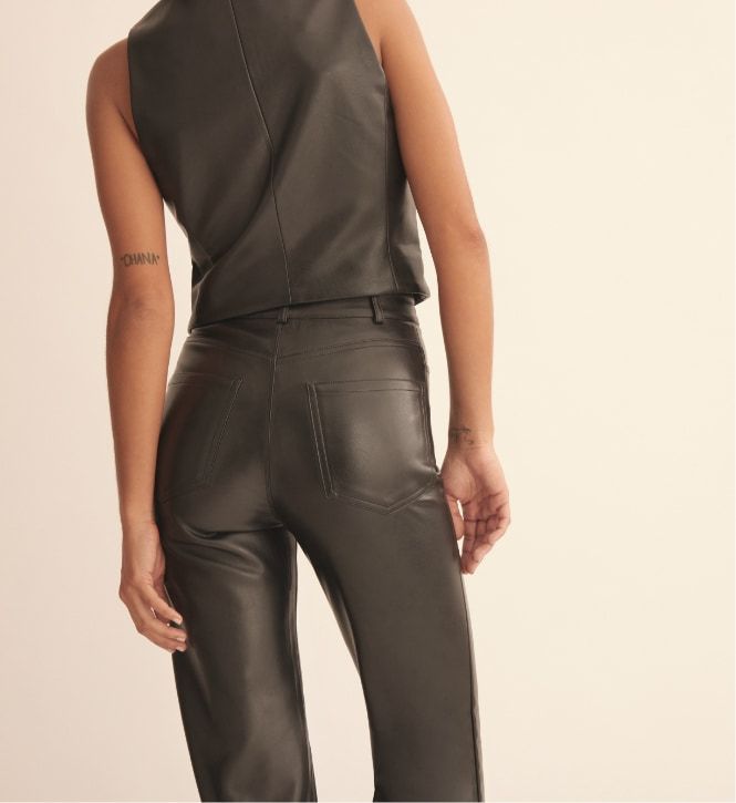 Une mannequin porte un pantalon droit ajusté en faux cuir noir et une veste sans manches en faux cuir noir.