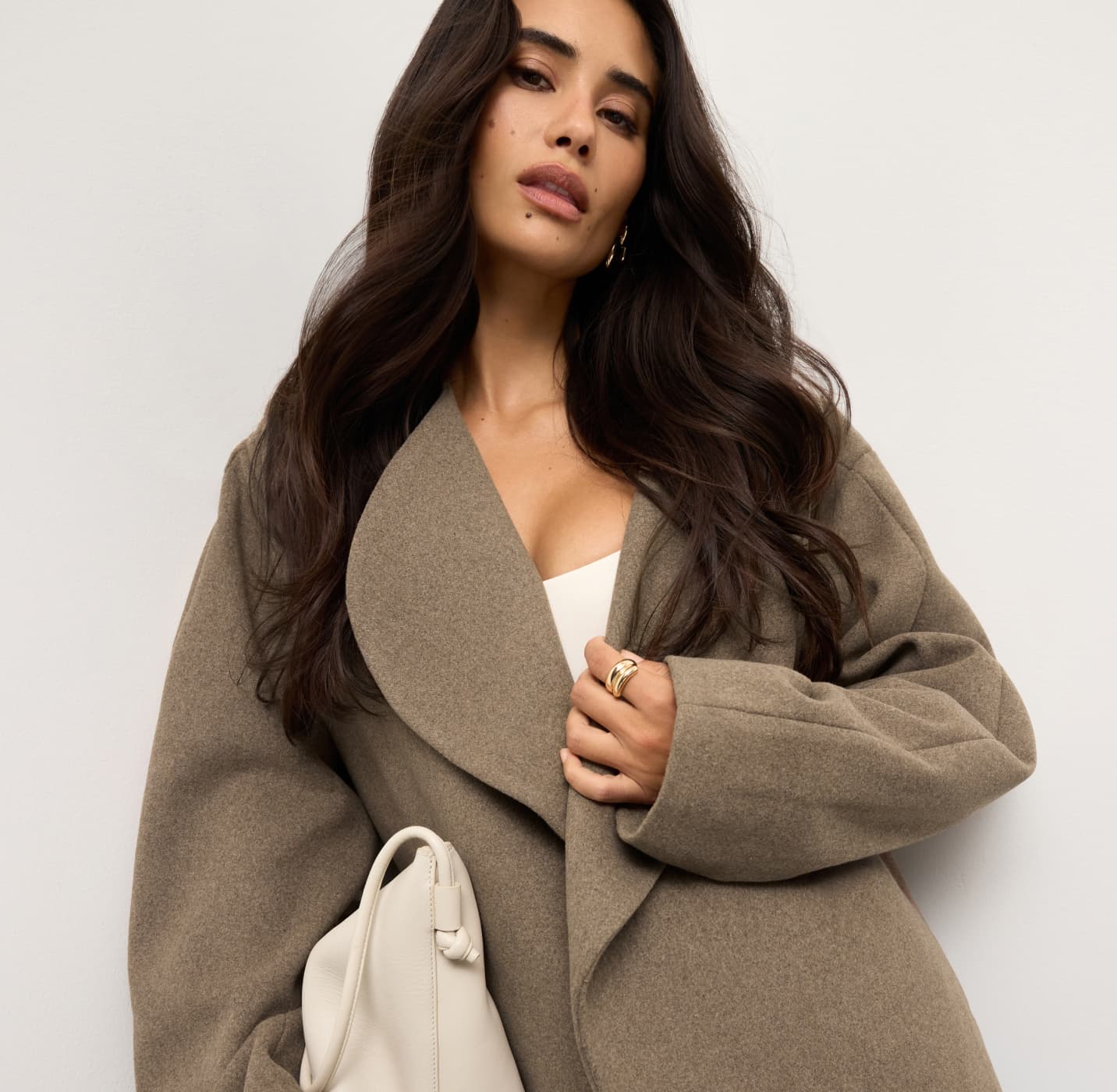 Model is wearing a brown wool coat over a white scoop tank top.
