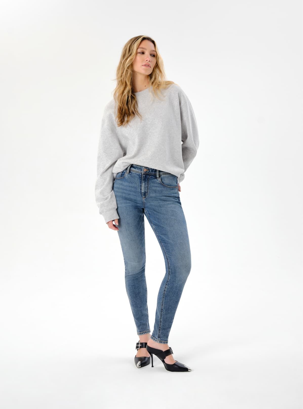 A model wears blue skinny jeans with a grey crewneck.