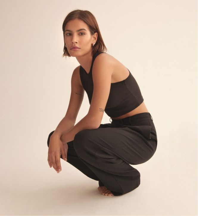 Une mannequin porte un pantalon noir à plis et une veste sans manches noire.