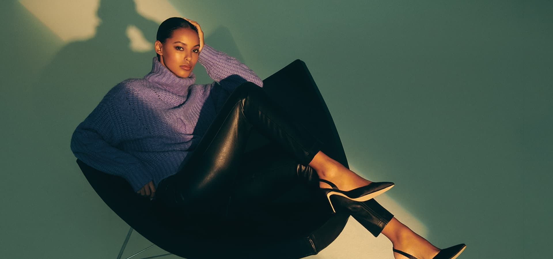 A model wears a purple turtleneck knit sweater with faux leather leggings.
