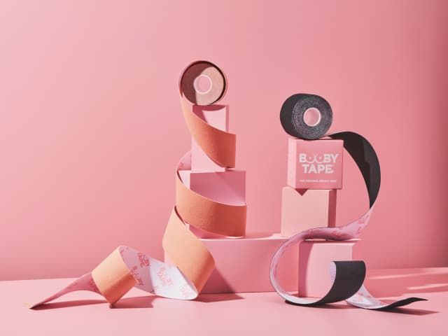 Produits Booby Tape présentés sur une toile de fond rose. 