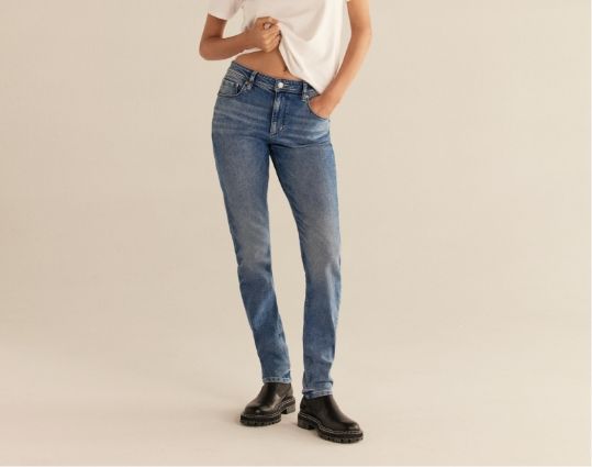 Une mannequin porte un jean bleu à taille mi-haute avec un t-shirt blanc