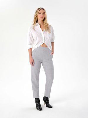 Une mannequin porte un pantalon gris à jambe étroite avec une chemise boutonnée blanche.