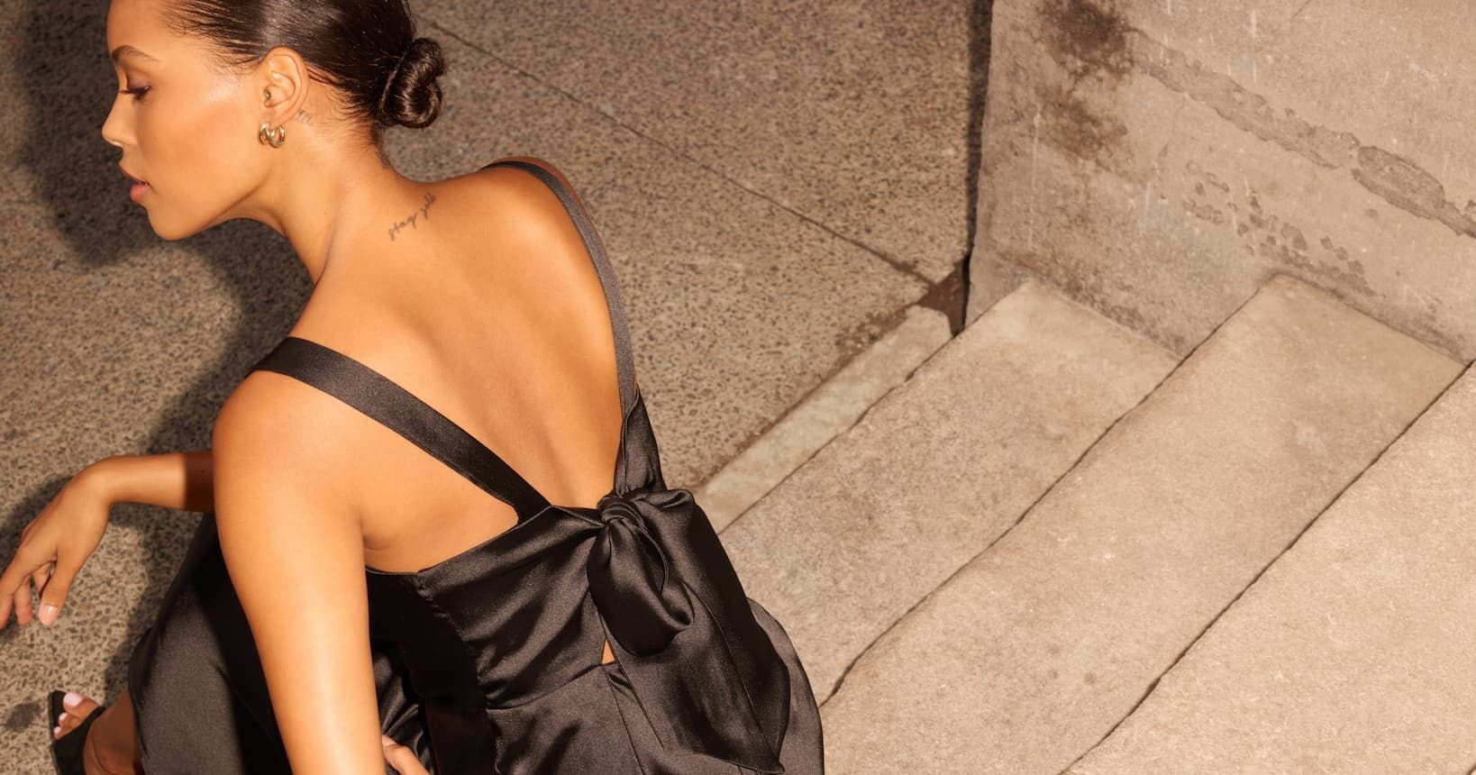 A model wears a black satin dress with a tie back.