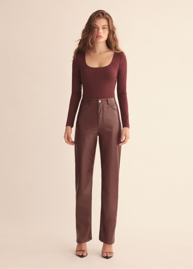 A model wears faux leather burgundy slim straight pants with a burgundy top.
