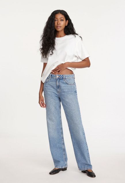 Model is wearing a white T-shirt and blue relaxed straight leg jeans.