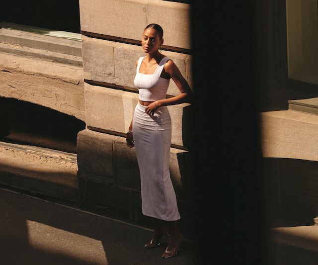 A model wears a white square neck tank top with a matching white midi skirt.