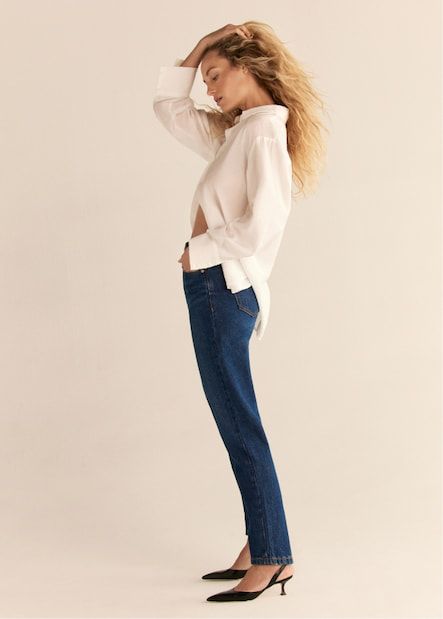 A model wears the Claudia mom jeans in dark indigo blue with a white button down shirt .
