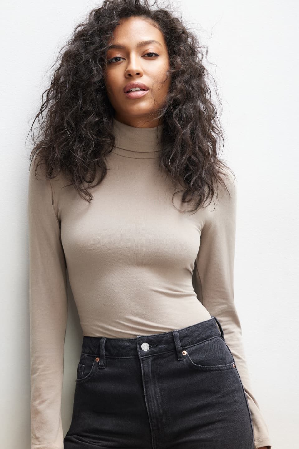 A model wears a beige long sleeve turtleneck with black jeans.